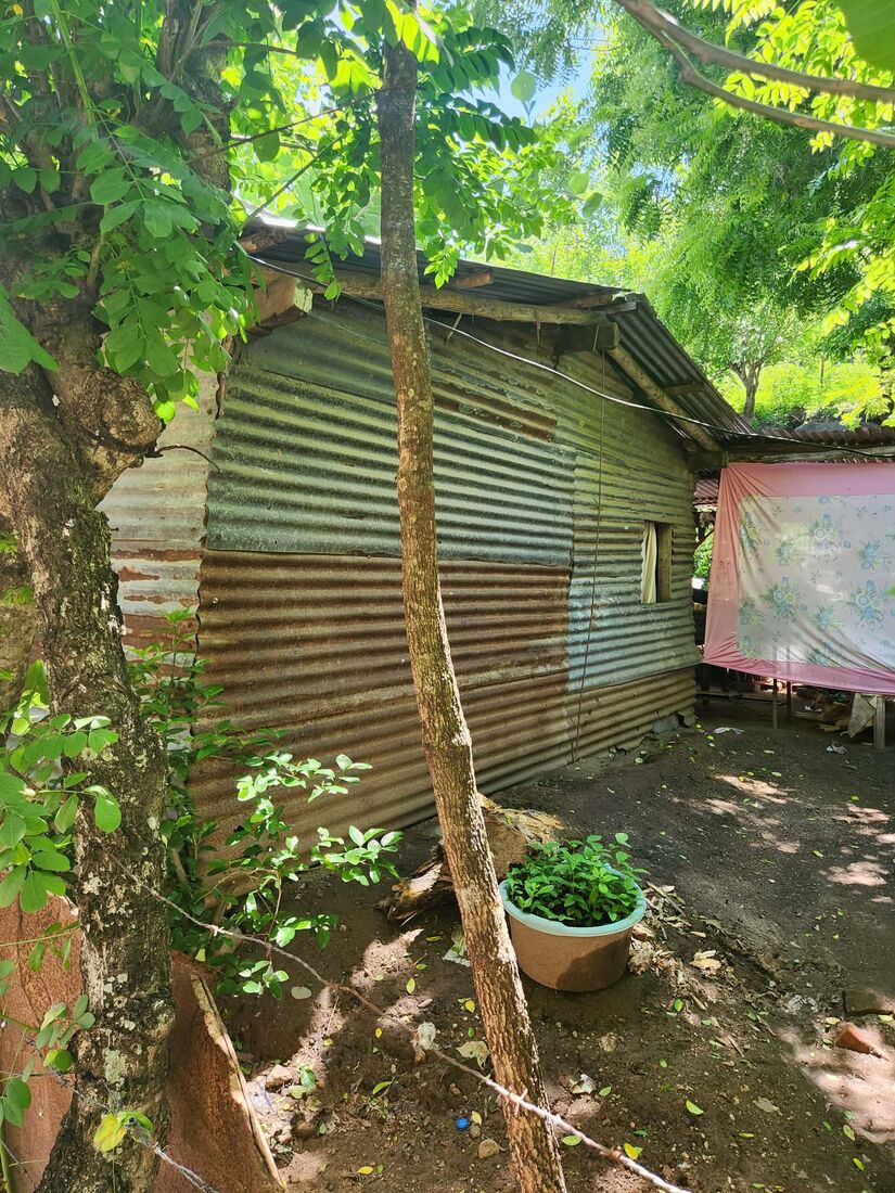 A home with corrugated metal walls and a plastic tarp serving as part of the wall, in a rural El Salvador yard