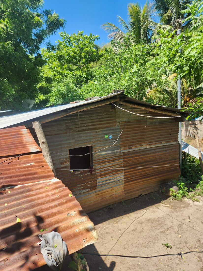 A small corrugated-metal home in El Salvador with a rusted exterior and a rough cut-out window, a candidate for 2026 repairs