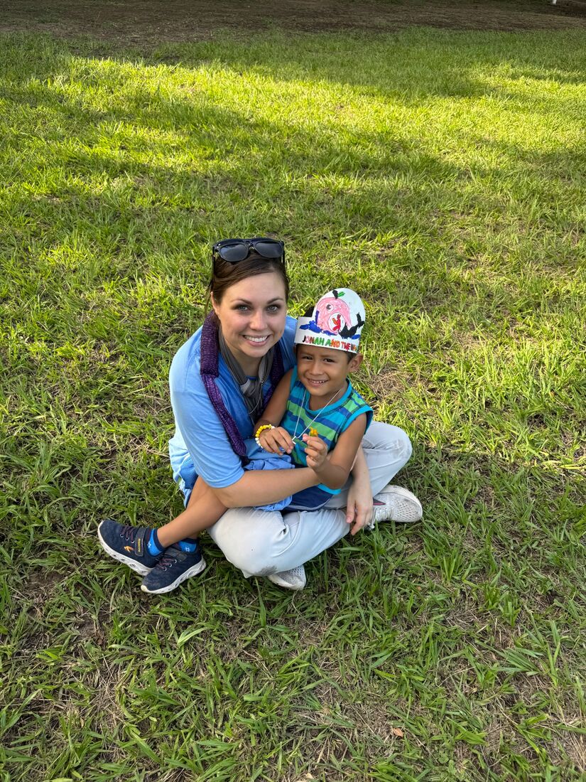 A team member kneeling on the grass with a smiling young child in El Salvador